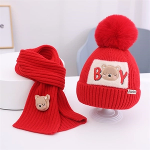 Nahaufnahme von rotem Strickset für Kinder mit Bären-Aufnäher und weichem Bommel-Detail