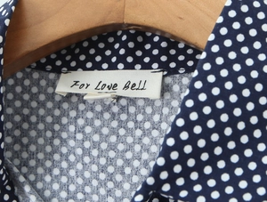Detail of navy blue polka dot blouse neckline with puff sleeves on a wooden hanger