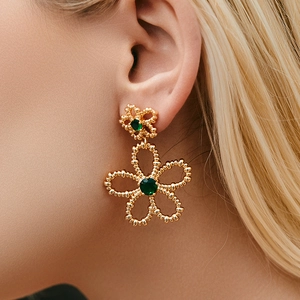 Elegant gold flower earrings with green crystals worn by a model in a side view