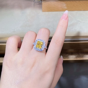 Close-up of radiant cut yellow diamond ring with white zircon halo on female hand