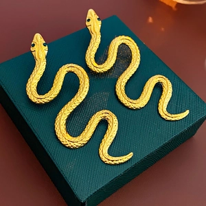 Detail of golden snake earrings with scale textures and green crystal eyes on a jewelry box