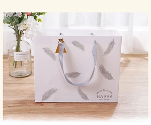 Detail of white gift bag with grey feather prints, satin handle and golden star charm