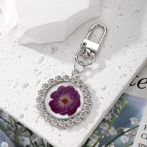 Detail shot of a silver key ring featuring a round pendant with purple dried flowers