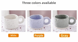 Detailed view of white, purple and grey ceramic mugs with large round handles and ink splatter