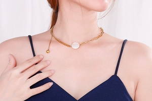 Close-up of asymmetric gold necklace with white shell pendant and tassel detail