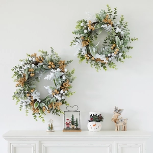 Set of two Christmas wreaths with gold berries and white leaves on a white fireplace