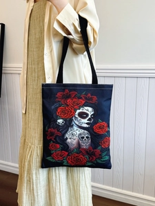 Black canvas tote bag with sugar skull and red rose print carried by a model on shoulder