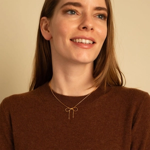 Close-up of minimalist gold bow pendant on thin snake chain worn by a model