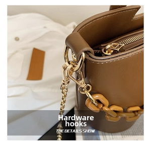 Close-up of golden hardware hooks and resin chain strap on a brown leather bag