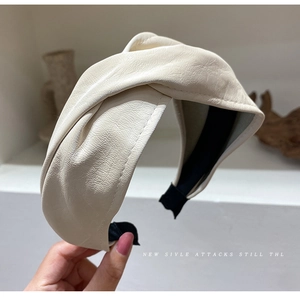 Detail of cream-colored wide faux leather headband featuring a stylish knotted design
