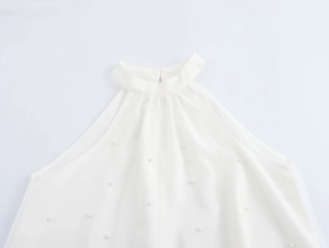 Detail eines weißen Neckholder-Tops mit eleganten Perlenverzierungen und Stehkragen