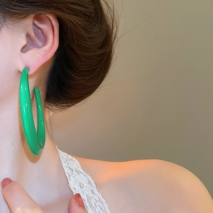 Detail of oversized bright green C-shaped hoop earrings in polished acrylic resin