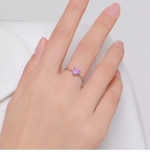 Close-up of pink heart-shaped opal ring with minimalist chain band design on finger