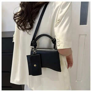 Détail d'un sac à main noir incurvé avec bandoulière réglable et petit porte-monnaie assorti