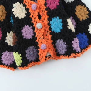 Detail of handmade black crochet cardigan with colorful floral patterns and pom-pom buttons