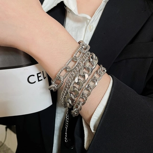 Detail of layered silver metal bracelets featuring Cuban and Figaro chain styles for women
