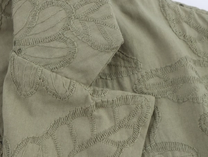 Close-up of olive green embroidered cotton fabric texture on hollow suit and pants