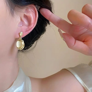 Detail of vintage gold earrings with cat's eye stone on female model ear lobe