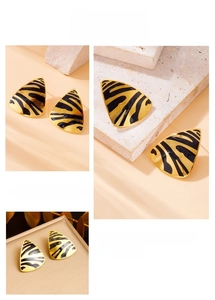 Detailed view of gold triangle earrings with black zebra enamel stripes on marble
