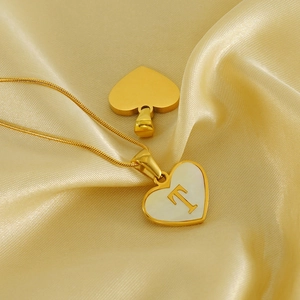 18K gold heart necklace with shell inlay and letter T on golden silk background