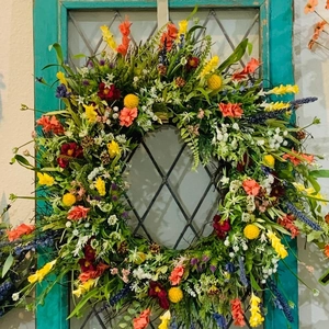 Colorful spring wildflower wreath with yellow and orange blooms hanging on a teal window