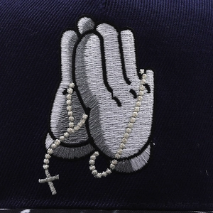 Detail of silver 3D embroidered praying hands and cross on navy blue baseball cap
