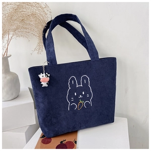 Detail of dark blue corduroy tote bag featuring rabbit embroidery and a cow pendant