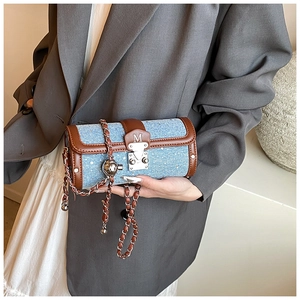 Detail of blue denim cylinder bag with brown leather trim and metallic chain strap