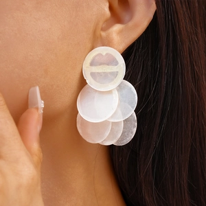 Close-up of white geometric shell earrings on a model showing natural resin textures