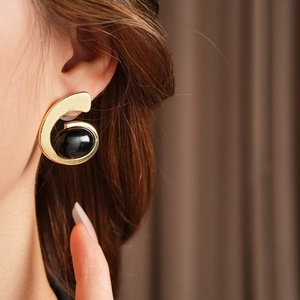 Vue détaillée de boucles d'oreilles dorées avec pierre ovale noire sur l'oreille