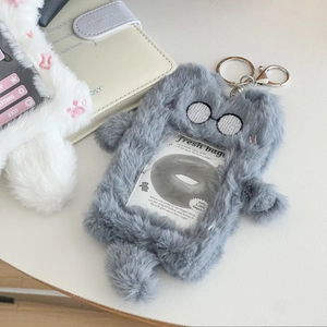 Detail of grey plush cat card holder with embroidery and a silver keychain on a desk
