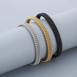 Detailed view of woven metal bracelets in gold, silver, and black on a cylinder