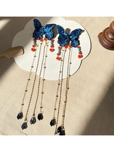 Détail d'une pince à cheveux papillon bleu avec pompons dorés et perles colorées