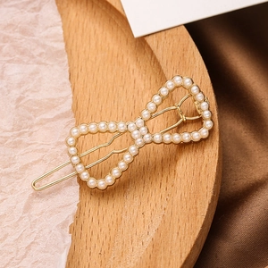 Golden hollow bow hair clip with faux pearl inlay on a natural wooden tray