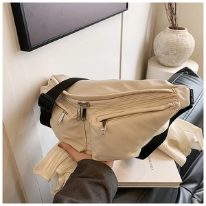 Detailed shot of a beige leather crossbody bag with wide strap in a minimalist setting