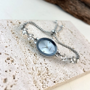 Detail of silver oval quartz watch featuring leaf-shaped diamond strap and adjustable clasp
