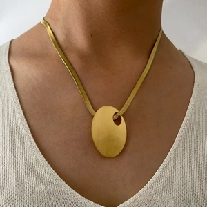 Golden snake chain necklace featuring a large brushed oval pendant worn by a model