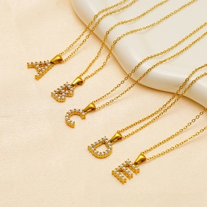 Macro shot of gold-plated A-E letter pendants featuring inlaid pearls on a beige surface