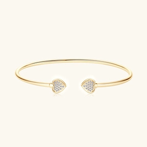 Detail van een gouden open armband met twee hartmotieven en micro-pave zirconia kristallen