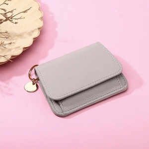 Close-up of grey leather short wallet with gold circular pendant on pink background