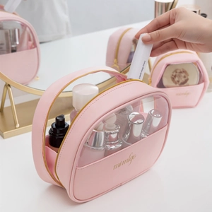 Pink PU leather half-moon makeup bag with transparent PVC panel on a bright vanity
