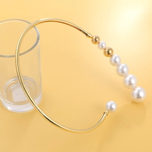Exaggerated golden metal choker with gradient white pearls on warm yellow backdrop