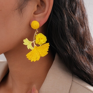 Bright yellow woven raffia flower and ginkgo leaf earrings worn by a female model