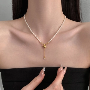 Détail d'un collier de perles avec pendentif gourde dorée et délicat pompon en métal