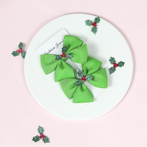 Close-up of two green Christmas bow hair clips with holly leaf decor on a display card