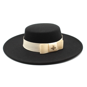 Detail of black wool fedora featuring a beige ribbon and golden bee metal ornament