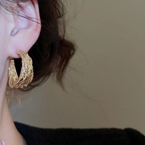 Detail of gold C-shaped earrings with woven texture worn for a vintage elegant look