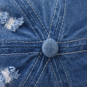 Detail of blue denim baseball cap showing top button stitching and distressed frayed edges