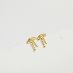 Detailed view of gold ribbon bow stud earrings on a minimalist white geometric stand