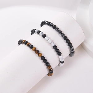 Detail of beaded morse code bracelets with natural tiger eye and matte stones on a white stand